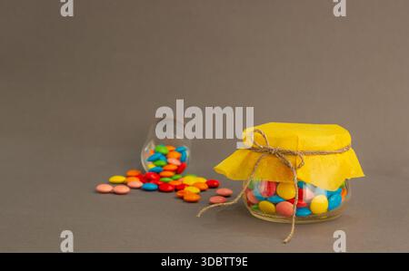 Schokoladenbonbons, klein, mehrfarbig in einem Glas mit Schleife. Stockfoto
