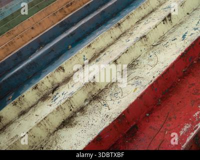 Nahaufnahme verwitterter, farbenfroher Bootsrümpfe und bemalter Stufen mit abblätternder Farbe und strukturierten Diagonalstreifen Stockfoto