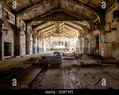 Sonnendurchflutete verlassene Fabrikinnenräume mit gewölbten Betonbögen und industriellem Verfall Stockfoto