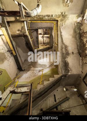 Verlassene Industrietreppe mit gelbem Geländer und abblätterndem Beton – vertikaler Blick auf das Innere einer verlassenen Fabrik Stockfoto