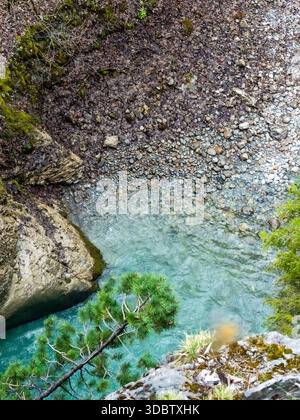 Blick aus der Vogelperspektive auf den türkisfarbenen Alpenfluss, der durch eine felsige Schlucht mit Kieselbett und Klippenrand fließt Stockfoto