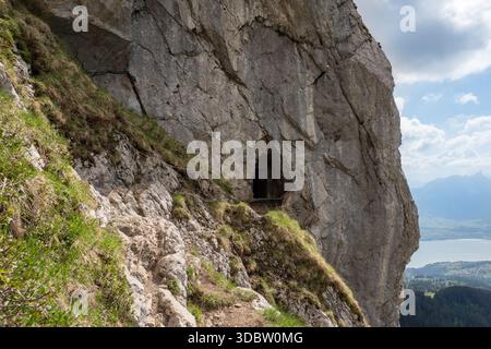 Felsenhöhle und schmaler Wanderweg am Sigriswiller Rothorn in den Schweizer Alpen mit Panoramablick auf See und Tal Stockfoto