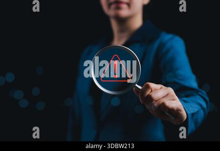 Konzept für Risikoerkennung und Warnmeldungen. Geschäftsfrau mit Lupe, die ein rotes Warnschild mit Ausrufezeichen hervorhebt, Stockfoto