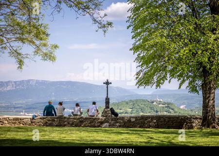 Der Blick auf eine ruhige aussicht entfaltet sich von einem grasbewachsenen Hügel, wo Figuren neben einer Steinmauer und einem Metallkreuz sitzen, eingerahmt von üppigen Bäumen, Grožnjan, County Istrien, Stockfoto