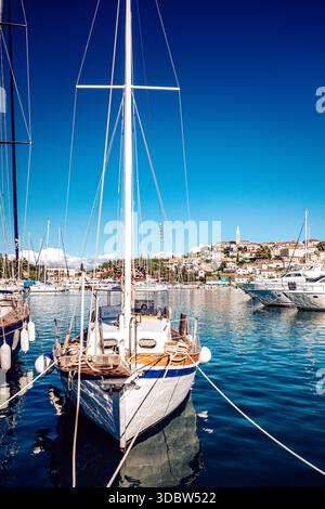 Blick auf ein Segelboot in einem ruhigen Hafen mit kristallblauem Wasser, das den Himmel reflektiert, vor der Kulisse einer bezaubernden Küstenstadt Vrsar, Stockfoto