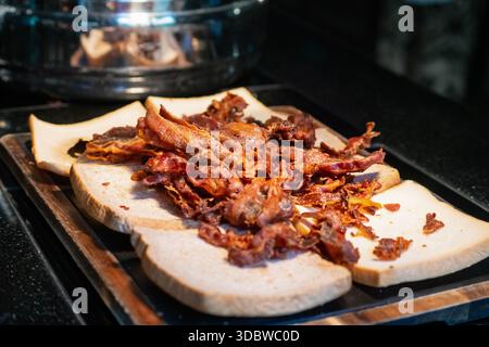 Eine Nahaufnahme knuspriger, goldbrauner gebratener Speck, serviert auf weichem weißem Brot. Aufgenommen unter warmer Beleuchtung an einer Frühstücksstation, Highli Stockfoto