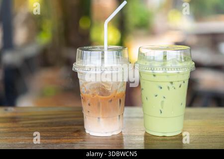 Zwei erfrischende Getränke zum Mitnehmen: Ein Eiskaffee Latte mit einem Strohhalm und ein geeister Matcha-grüner Tee. Auf einem rustikalen Holztisch in einem Café im Freien Stockfoto