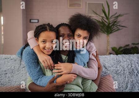 Glückliche Schwarze Mutter, die ihre beiden Töchter lächelnd umschließt Stockfoto