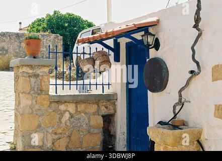 Traditioneller Innenhof aus Stein mit blauer Tür, hängenden Körben und Terrakotta-Topf in mediterranem Licht, Insel Agistri, Griechenland Stockfoto