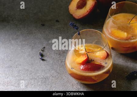 Pfirsich kalte Limonade oder Bellini Cocktail mit Lavendelblüten diente in zwei Gläser auf dunklen Textur Tabelle. Hausgemachte Sommer trinken. Stockfoto