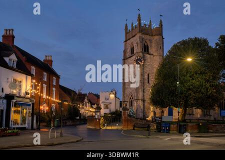 St. Nikolaus Kirche und Häuser entlang der Butterstraße in der Abenddämmerung im dezember. Alcester, Warwickshire, England Stockfoto