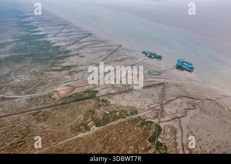 Aus der Vogelperspektive sehen Sie Boote, die an der matschigen Küste liegen, wo geometrische Muster in die Erde eingeätzt und die gedämpften Töne des Horizonts, Chattogram, Chittagong, treffen Stockfoto