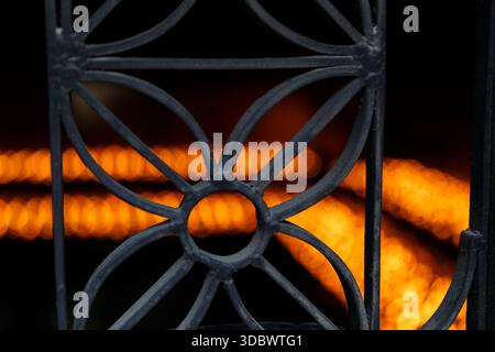 Glühende Tempelöllampen, die durch einen eisernen Grill gesehen werden, schaffen einen warmen abstrakten Hintergrund mit Feuerlicht und traditioneller Atmosphäre. Stockfoto