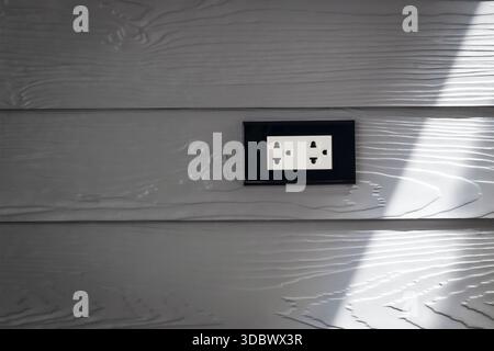 Steckdose an strukturierter grauer Wandplatte mit Schatten Stockfoto