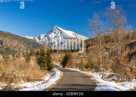 Krivan-Berg im Nationalpark hohe Tatra, Slowakei, Europa. Die malerische Straße schlängelt sich durch eine bewaldete Landschaft in Richtung eines schneebedeckten Berggipfels Stockfoto