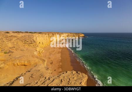 Blick auf goldene Klippen treffen auf das türkisfarbene Meer unter einem klaren Himmel, mit Wellen, die die Sandküste küssen, eine ruhige Küstenszene, Gwadar, Belutschistan, Pak Stockfoto