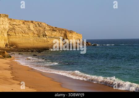 Blick auf goldene Klippen treffen auf das türkisfarbene Meer, die Wellen küssen sanft die Sandküste unter klarem Himmel, Gwadar, Belutschistan, Pakistan. Stockfoto