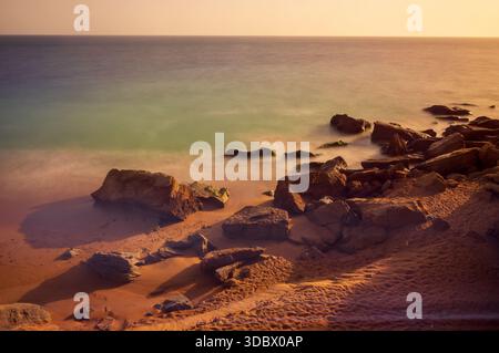 Blick auf die Küste mit Felsen und Meer während Sonnenuntergang, die einen warmen Glanz auf den Sand, Gawadar, Belutschistan, Pakistan. Stockfoto
