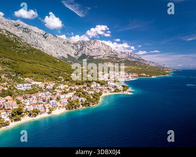 Aus der Vogelperspektive auf die sonnenverwöhnte Küste, wo Terrakotta-Dächer auf die türkisfarbene Adria treffen, eingerahmt von den majestätischen Biokovo-Bergen, Brela, Split- Stockfoto