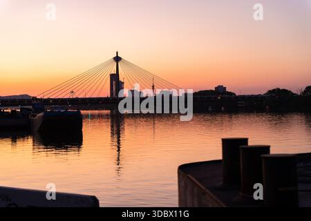 Der Blick auf die Donau spiegelt die feurigen Farben des Sonnenuntergangs wider und strahlt ein goldenes Leuchten über die Brücke und das Stadtbild in Wien, Wien, Österreich. Stockfoto