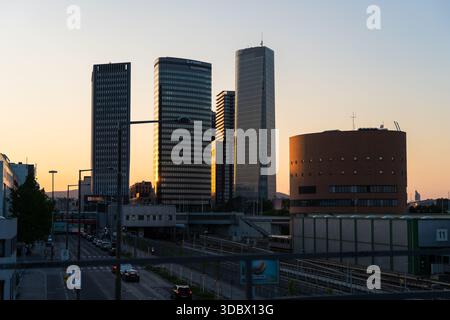 Blick auf moderne Wolkenkratzer, die den Dämmerungshimmel durchdringen, während die Sonne unter dem Horizont untergeht und goldene Farbtöne auf die urbane Landschaft, Wien, Au, wirft Stockfoto
