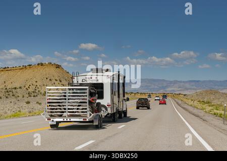 Moab, Utah, USA - 26. Mai 2025: Alter Geländewagen auf einem Anhänger hinter einem Pick-up-Truck, der einen Wohnmobil auf einer Autobahn in der Nähe von Moab zieht Stockfoto