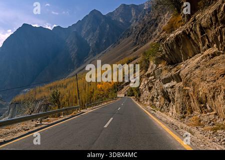 Blick auf eine lange Straße, die durch zerklüftete Berge führt, mit ein paar herbstbunten Bäumen, die sich an den steilen Hängen hängen, Hunza, Gilgit Baltistan, Pakistan. Stockfoto