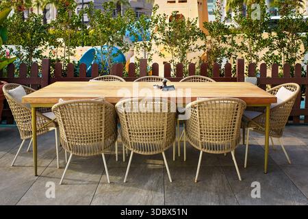 Familien-Freizeitbereich mit großem Esstisch mit reserviertem Schild und Korbstühlen auf einer modernen Restaurantterrasse mit Spielplatz-Hintergrund. Stockfoto