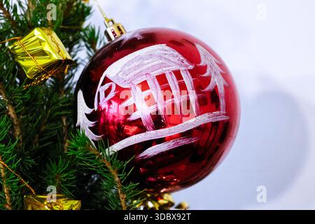 Rote Weihnachtskugel mit weißem Haus-Design auf einem grünen Baum Stockfoto