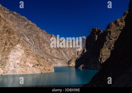 Der Blick auf das türkisfarbene Wasser fließt ruhig zwischen hoch aufragenden, sonnendurchfluteten, felsigen Bergen unter einem tiefblauen Himmel und schafft einen auffälligen Kontrast von Farbe und Text Stockfoto