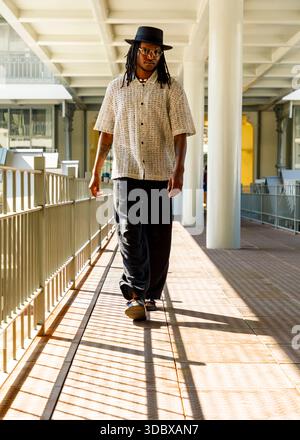 Ein Mann mit Hut, Brille und gemustertem Hemd läuft einen Gang hinunter. Stockfoto