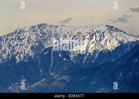 Blick auf eine majestätische, schneebedeckte Bergkette, deren Gipfel vom sanften Licht der Sonne geküsst werden und einen atemberaubenden Kontrast zum tiefblauen Himmel schaffen. Stockfoto