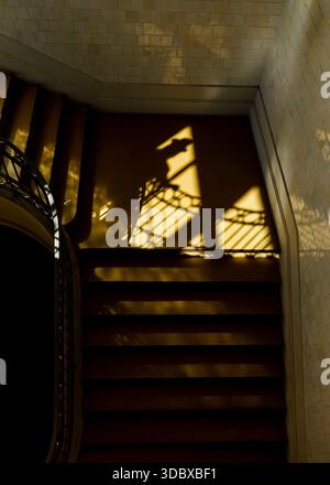 Ein Blick von oben nach unten auf eine Treppe mit Schatten über sie. Die Schatten scheinen von einem dekorativen Geländer und einem Fenster zu stammen. Stockfoto