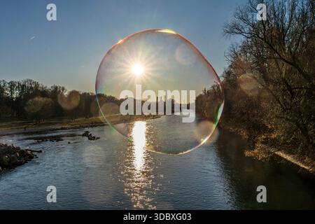 Poesie in der Seifenblase, die tiefstehende Wintersonne taucht die Isar in ein magisches Licht, München, 18. Dezember 2025 Deutschland, München, 18. Dezember. Dezember 2025, Poesie in der Seifenblase, wie durch eine gläserne Christbaumkugel strahlt die tiefstehende Wintersonne und taucht die Isar in einem magischen Licht, ein strahlender Wintertag geht zu Ende, das Heizkraftwerk Süd am Horizont, ein Mann auf der Reichenbachbrücke lässt die Seifenblasen zur Freude der Passanten in den blauen Himmel steigen, Donnerstagnachmittag, Temperaturen um die 10 Grad, Weihnachtszeit, Adventszeit, Winter, Sonniges Win Stockfoto
