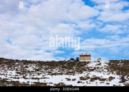 Ein einsames Steinhaus am Hang eines schneebedeckten Berges in der Nähe des Gletschersees Ercina. Covadonga Lakes, Picos de Europa, Asturien, Spanien. Stockfoto