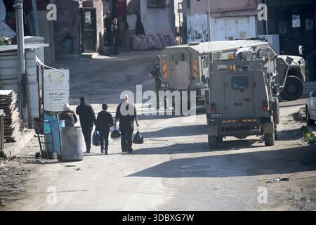 Nablus, Palästina. Dezember 2025. Eine palästinensische Familie läuft bei einem Angriff auf das Flüchtlingslager Askar östlich von Nablus im Westjordanland an Militärfahrzeugen vorbei. Israelische Truppen plünderten palästinensische Häuser und Geschäfte im Lager auf der Suche nach palästinensischen Militanten. Ein Palästinenser wurde bei der Suche verletzt. Quelle: SOPA Images Limited/Alamy Live News Stockfoto