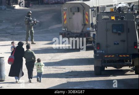 Nablus, Palästina. Dezember 2025. Eine palästinensische Familie läuft bei einem Angriff auf das Flüchtlingslager Askar östlich von Nablus im Westjordanland an Militärfahrzeugen vorbei. Israelische Truppen plünderten palästinensische Häuser und Geschäfte im Lager auf der Suche nach palästinensischen Militanten. Ein Palästinenser wurde bei der Suche verletzt. Quelle: SOPA Images Limited/Alamy Live News Stockfoto