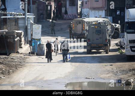 Nablus, Palästina. Dezember 2025. Eine palästinensische Familie läuft bei einem Angriff auf das Flüchtlingslager Askar östlich von Nablus im Westjordanland an Militärfahrzeugen vorbei. Israelische Truppen plünderten palästinensische Häuser und Geschäfte im Lager auf der Suche nach palästinensischen Militanten. Ein Palästinenser wurde bei der Suche verletzt. Quelle: SOPA Images Limited/Alamy Live News Stockfoto