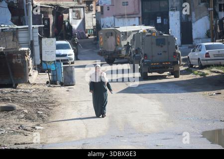 Nablus, Palästina. Dezember 2025. Eine Palästinenserin läuft bei einem Angriff auf das Flüchtlingslager Askar östlich von Nablus im Westjordanland an israelischen Militärfahrzeugen vorbei. Israelische Truppen plünderten palästinensische Häuser und Geschäfte im Lager auf der Suche nach palästinensischen Militanten. Ein Palästinenser wurde bei der Suche verletzt. Quelle: SOPA Images Limited/Alamy Live News Stockfoto