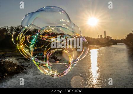 Die tiefstehende Wintersonne taucht die Isar in ein magisches Licht, eine Seifenblase schillert im Licht, München, 18. Dezember 2025 Deutschland, München, 18. Dezember. Dezember 2025, in schillernden Regenbogenfarben leuchtet eine Seifenblase in der Wintersonne, über der Isar wölbt sich ein strahlend blauer Himmel, ein sonniger Wintertag geht zu Ende, das Heizkraftwerk Süd am Horizont, ein Mann auf der Reichenbachbrücke lässt die Seifenblasen zur Freude der Passanten in den Himmel steigen, Donnerstagnachmittag, Temperaturen um die 10 Grad, Weihnachtszeit, Adventszeit, Winter, sonniges Winterwetter, Baye Stockfoto