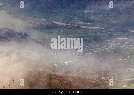 Blick auf eine von Nebel gehüllte Landschaft, wo grüne Felder auf die Ausläufer treffen und der Himmel sich mit der Erde verschmilzt, Muzaffarabad, Azad Kaschmir, Pakistan. Stockfoto