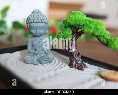 Buddha-Statue im Zen-Stil. Miniatur-Meditations- und Entspannungsset für Zuhause auf dem Tisch. Östlicher Steingarten. Stockfoto