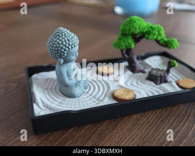 Buddha-Statue im Zen-Stil. Miniatur-Meditations- und Entspannungsset für Zuhause auf dem Tisch. Östlicher Steingarten. Stockfoto