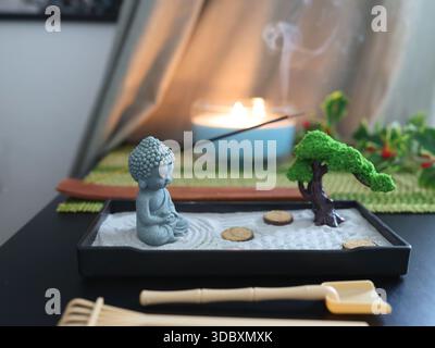 Buddha-Statue im Zen-Stil. Miniatur-Meditations- und Entspannungsset für zu Hause auf dem Tisch mit Räucherstäbchen am Ständer. Östlicher Steingarten. Stockfoto