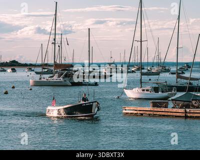Ein kleines Motorboot fährt bei ruhigen Sommerbedingungen durch ein Anlegefeld für Segelboote in Port Jefferson Harbor, Suffolk County, New York. Stockfoto