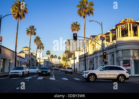 Rodeo Drive und Santa Monica Boulevard bei Sonnenuntergang mit Autos auf der berühmten Straße in Beverly Hills, Los Angeles, mit Palmen und Geschäften Stockfoto