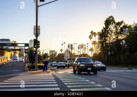 Santa Monica Boulevard und Rodeo Drive bei Sonnenuntergang mit Autos auf der berühmten Straße in Beverly Hills, Los Angeles, mit hinterleuchteten Palmen Stockfoto