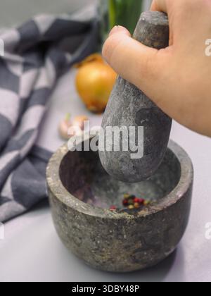 Lebensmittelzubereitung Nahaufnahme mit Handmahlen von Pfefferkörnern in Steinmörtel Stockfoto