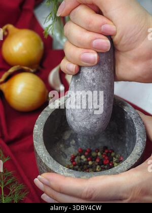 Nahaufnahme der Hände mit Steinmörtel und Stößel mit Pfefferhörnern zum Kochen Stockfoto