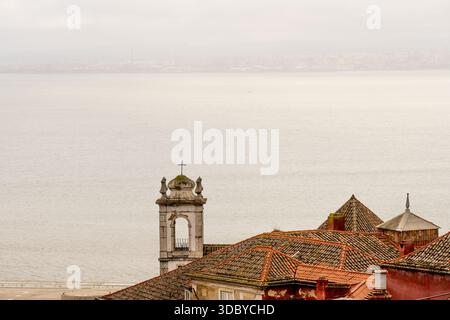 Lissabon Portugal 5. Dezember 2025 Dächer und ein Kirchturm erscheinen über dem Fluss bei weichem Tageslicht Stockfoto